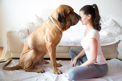 Side view of young woman face to face with dog sitting on bed at home