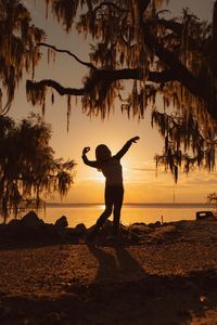 Silhouette girl dancing at beach against sky during sunset
