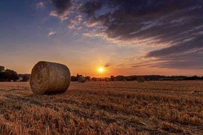 Hay bales on field against sky during sunset