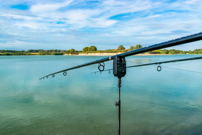 Fishing rod by lake against sky