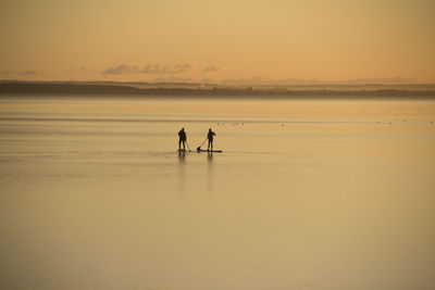 Silhouette people on beach against sky during sunset