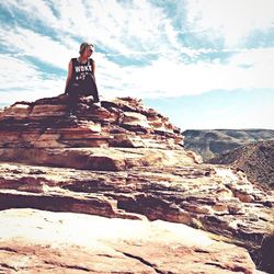 Woman sitting on rock against sky
