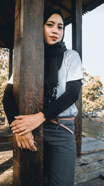 Portrait of young woman standing by pole outdoors