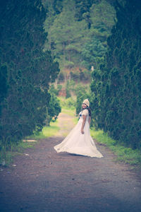 Bride wearing wedding dress standing amidst trees on walkway