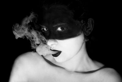 Close-up portrait of shirtless woman smoking against black background