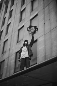 Low angle view of woman holding umbrella against building in city