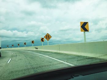 Arrow symbols on highway against cloudy sky seen through windshield