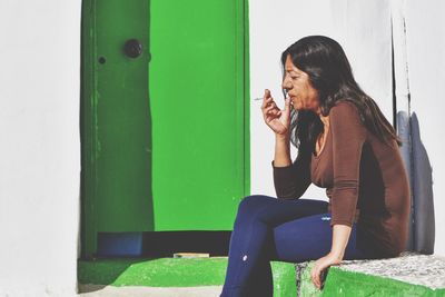 Mature woman smoking cigarette while sitting on retaining wall