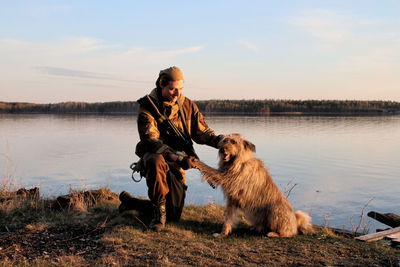 Man with dog by lake against sky