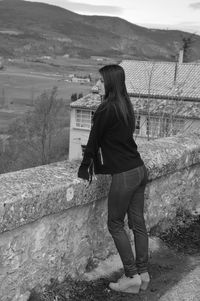 Woman standing by retaining wall against landscape