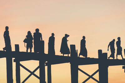 Silhouette people walking on railing against sky during sunset