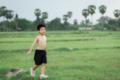 Full length of shirtless boy standing on field