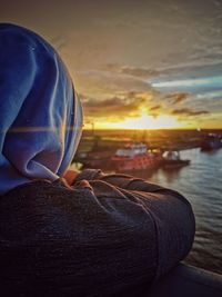 Close-up of person by sea against sky during sunset