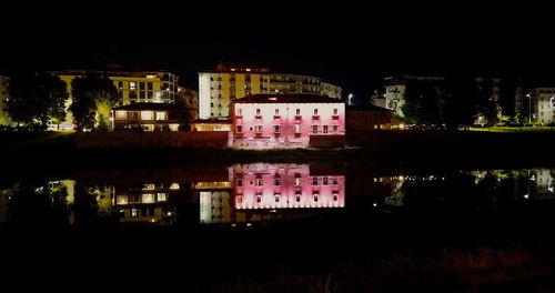 Illuminated buildings by lake against sky in city at night