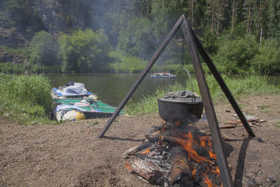 Camping stove hanging over bonfire against river at forest