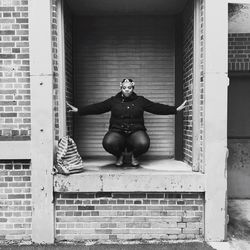 Portrait of woman crouching against shutter