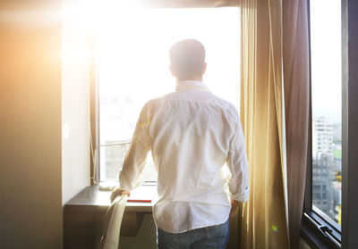 Rear view of man looking through window at home