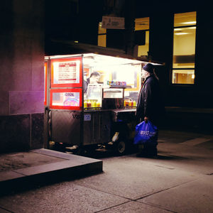 Rear view of man walking on illuminated street at night