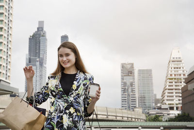 Portrait of smiling young woman standing against buildings in city