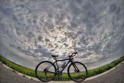 Bicycle by road against cloudy sky