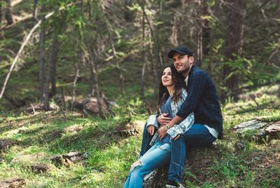 Couple looking away while sitting on rock in forest