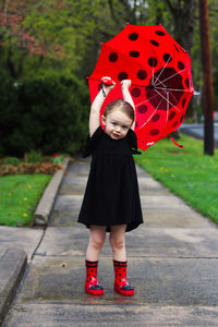 Full length portrait of cute girl standing with umbrella on footpath