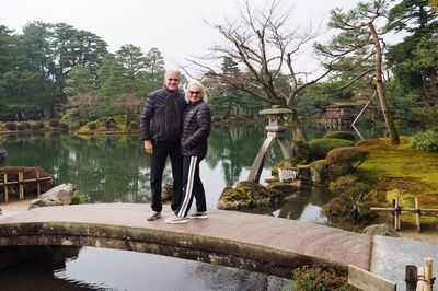 Portrait of happy mature couple standing on footbridge over pond at kenroku-en