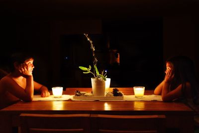 Side view of siblings sitting at restaurant table in dark