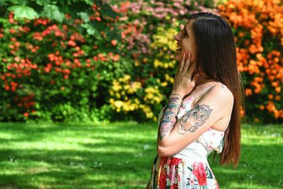 Side view of young woman standing against plants