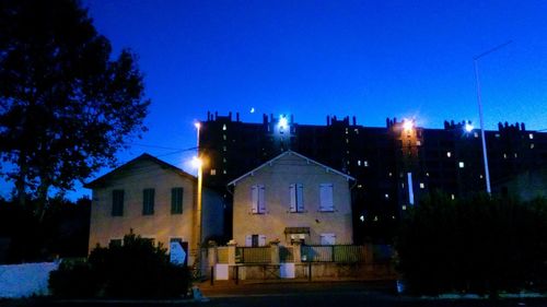 Illuminated houses against clear blue sky at night