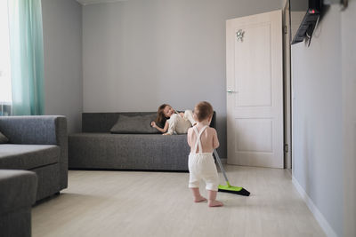 Children siblings with mop sweep floor in bright living room, housework and sibling relationships