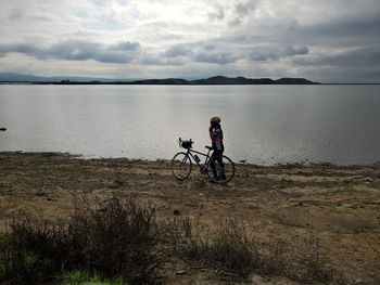 Man riding bicycle on shore against sky