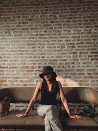 Young woman sitting against brick wall