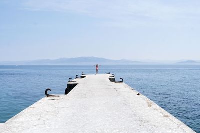 Woman standing on pier amidst sea against sky