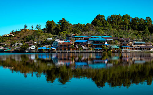 Scenic view of lake by village against blue sky