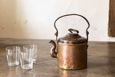 Still life with a beautiful worn retro style copper tea kettle with empty glasses on a wooden table.