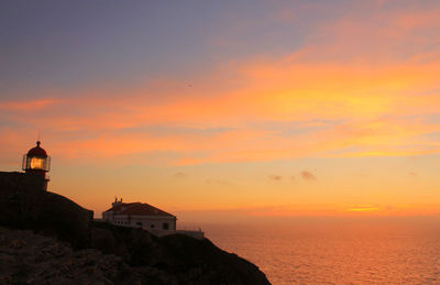 Silhouette built structure by sea against orange sky