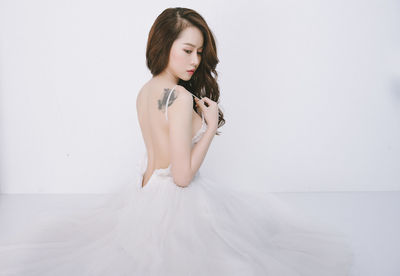 Young woman sitting on wall against white background