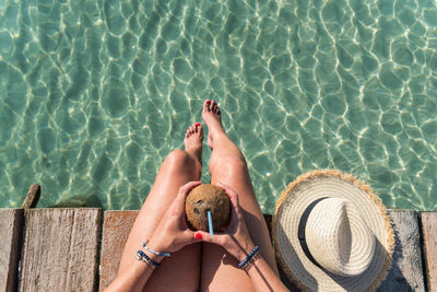 From above of unrecognizable female sitting with coconut cocktail with straw near blue rippling sea and enjoying summer holiday on playa de muro