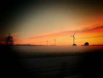 Silhouette of wind turbines on field at sunset