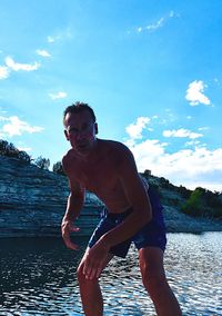 Portrait of shirtless man bending against sea and sky