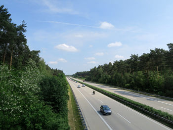 Cars on highway amidst trees against sky