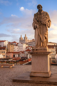 Statue against buildings in city during sunset