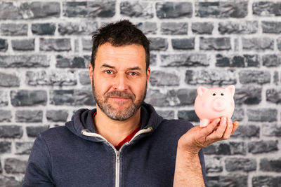 Man holds a piggy bank in his hand against a stone wall