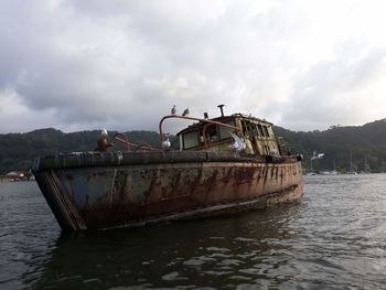 Abandoned boat moored in river against sky