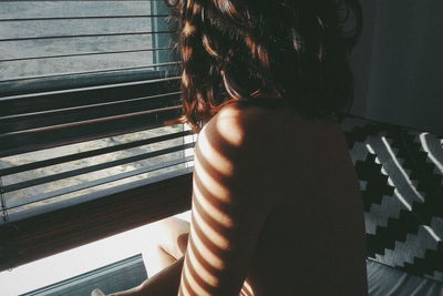 Close-up of sensuous topless woman sitting on bed by window at home