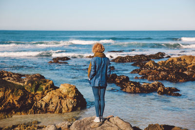 Rear view of mid adult woman standing at rocky shore