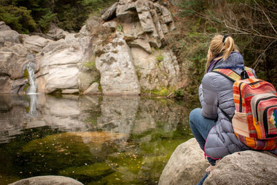 Rear view of woman sitting on rock by river