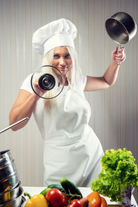 Portrait of young woman holding utensils while standing in kitchen