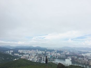 Rear view of woman standing on hill while looking at cityscape against sky